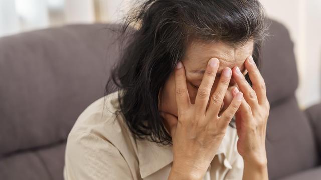 Eine Frau hält ihren Kopf mit geschlossenen Augen in den Händen
