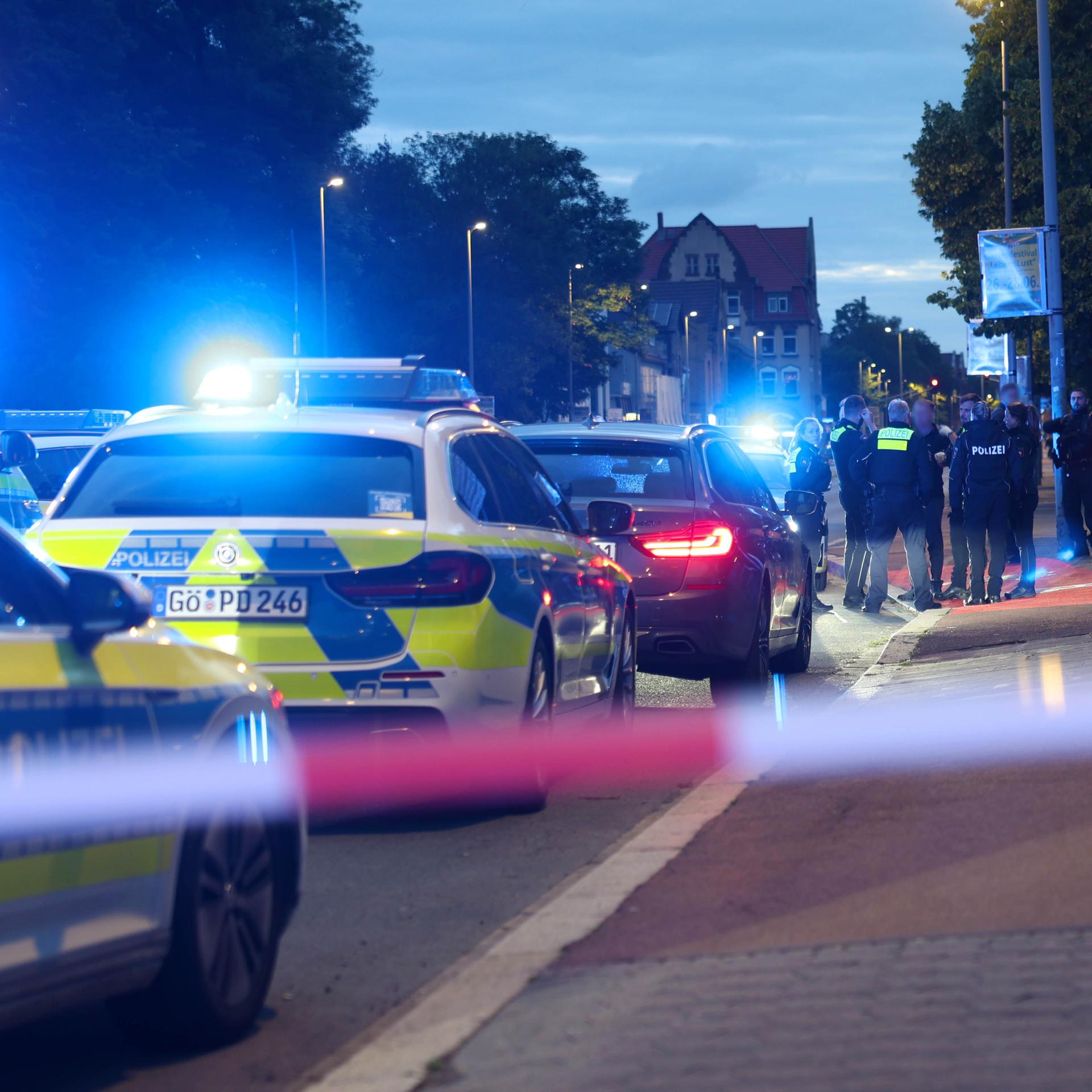 Polizisten und Polizeifahrzeuge stehen hinter einer Absperrung. Ein Polizist ist bei einer Auseinandersetzung zwischen zwei Personengruppen im niedersächsischen Göttingen angeschossen worden. 