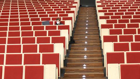 An der Universität Leipzig sitzt ein Informatikstudent bei einer digitalen Vorlesung allein im Auditorium maximum. Er blickt auf seinen Laptop, die Stuhlreihen sind sonst leer.