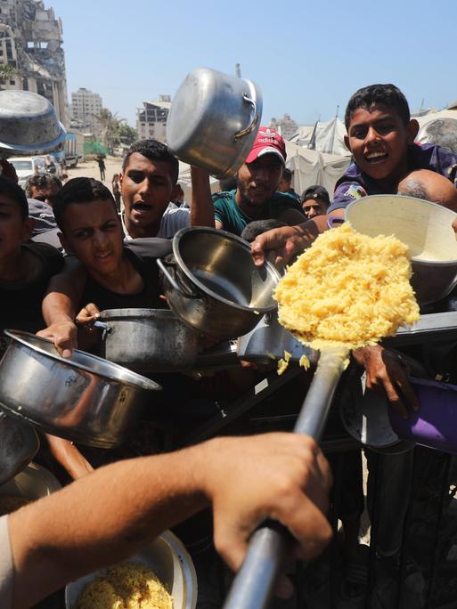 Palästinenser mit leeren Töpfen in der Hand bei einer Essenverteilung in Gaza