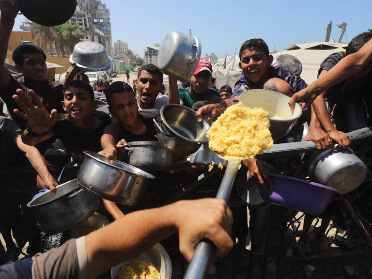 Palästinenser mit leeren Töpfen in der Hand bei einer Essenverteilung in Gaza