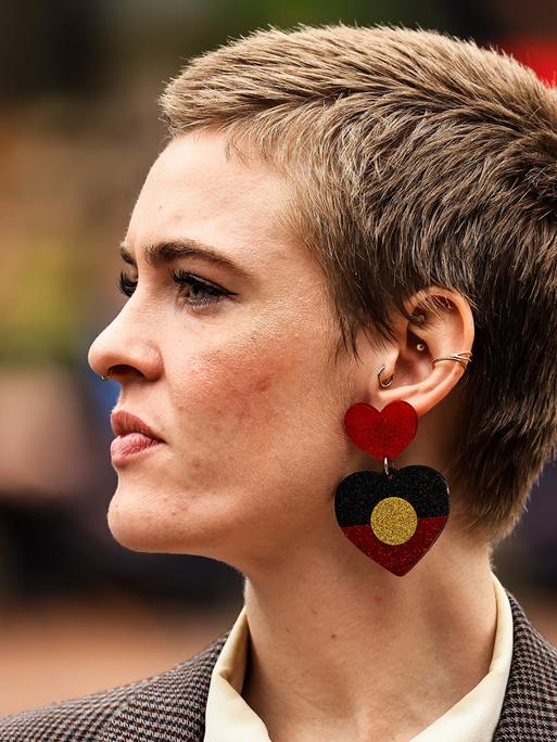 Eine junge Frau mit kurzen Haaren und mit Ohrringen in Herzform, die die Flagge der Aborigines zeigt, ist von der Seite zu sehen.