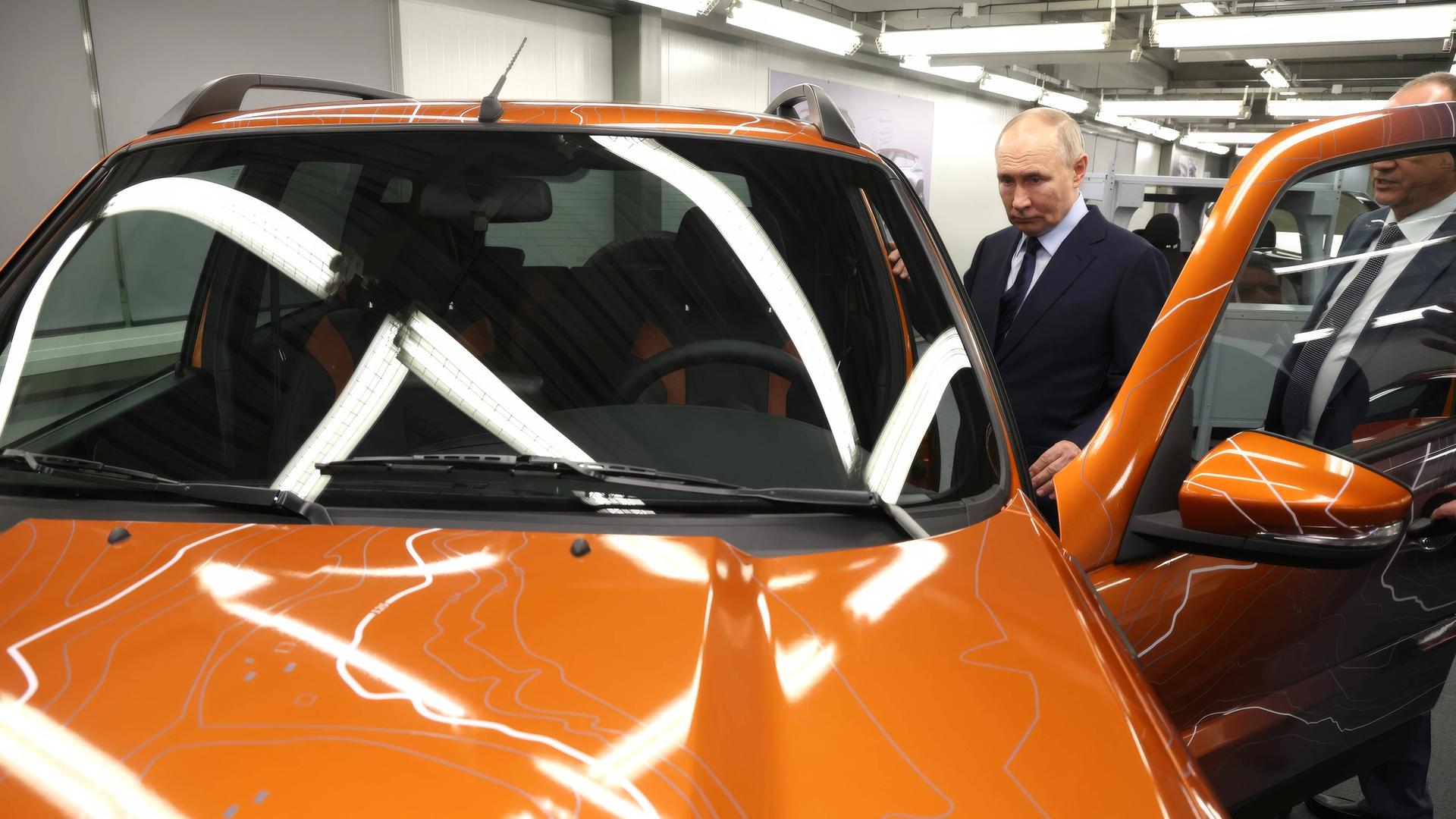 Der russische Präsident Putin steht neben einem orangenen Auto während eines Besuchs in einer Autofabrik.