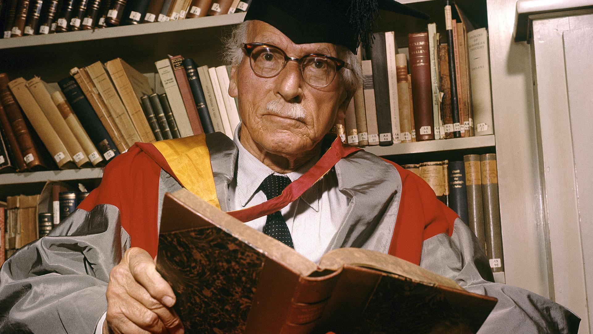 Der Schweizer Psychotherapeut Carl Gustav Jung sitzt in einem Sessel, auf dem Schoß ein Buch.