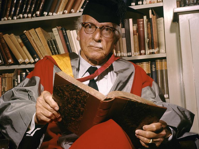 Der Schweizer Psychotherapeut Carl Gustav Jung sitzt in einem Sessel, auf dem Schoß ein Buch.