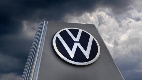 Das VW-Logo an der Wand von einem großen Haus. Über dem Haus sind dunkle Wolken.