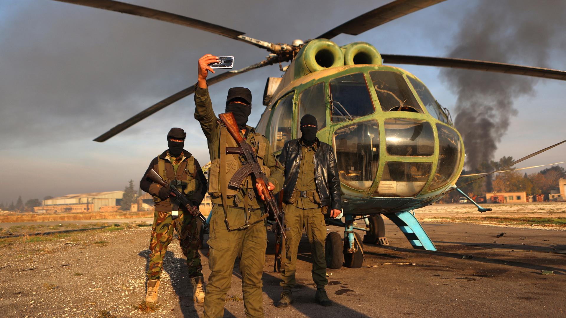 Dschihadistische Rebellen posieren für ein Selfie vor einem Armeehubschrauber auf dem Rollfeld des Militärflughafens Nayrab in der nordsyrischen Stadt Aleppo am 2. Dezember 2024.