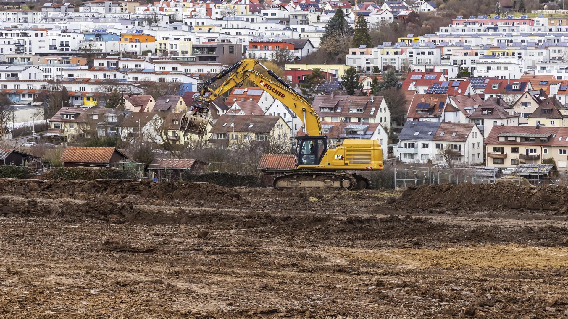 Ein Bagger steht auf Ackerland. Im Hintergrund sieht man mehrere Häuser. Ein Bagger steht auf Ackerland. Im Hintergrund sieht man mehrere Häuser.