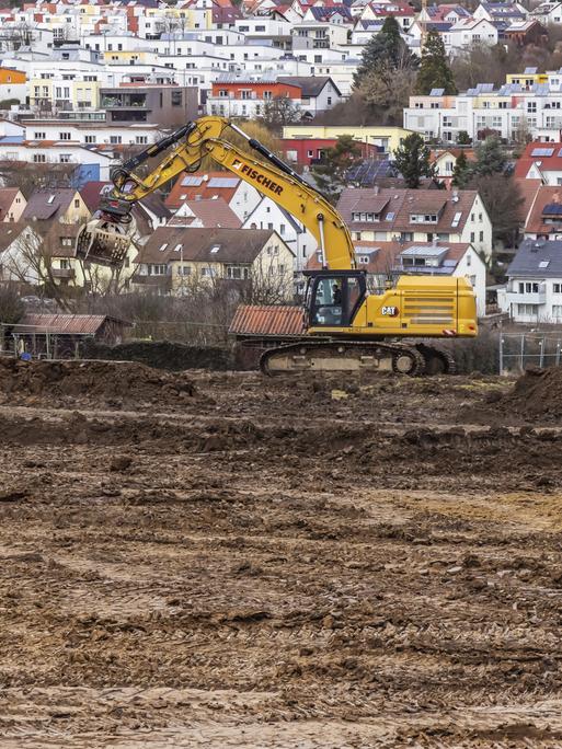 Ein Bagger steht auf Ackerland. Im Hintergrund sieht man mehrere Häuser. Ein Bagger steht auf Ackerland. Im Hintergrund sieht man mehrere Häuser.