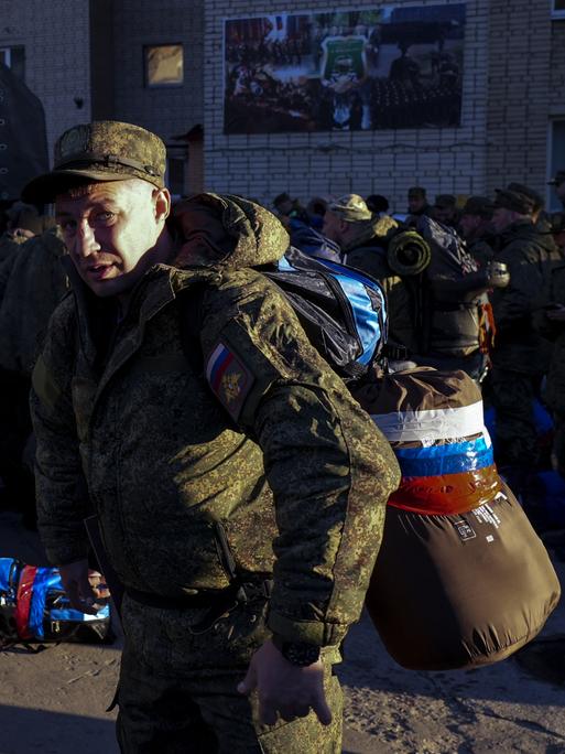 Zu sehen ist ein Mann in Militäruniform mit Schlafsack und Gepäck das mit Tape in den Farben der russischen Flagge zusammengeklebt wurde.

