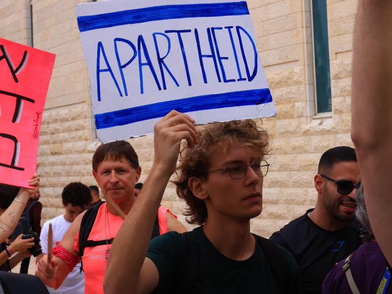 Israelische Aktivisten protestieren, einer hälten ein Schild mit der Aufschrift "Apartheid" hoch Israelische Aktivisten protestieren, einer hälten ein Schild mit der Aufschrift "Apartheid" hoch