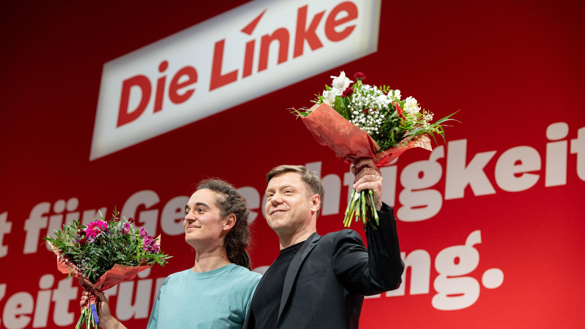 Carola Rackete und Martin Schirdewan stehen während des Bundesparteitages der Linken auf der Bühne und halten Blumensträuße in der Hand.