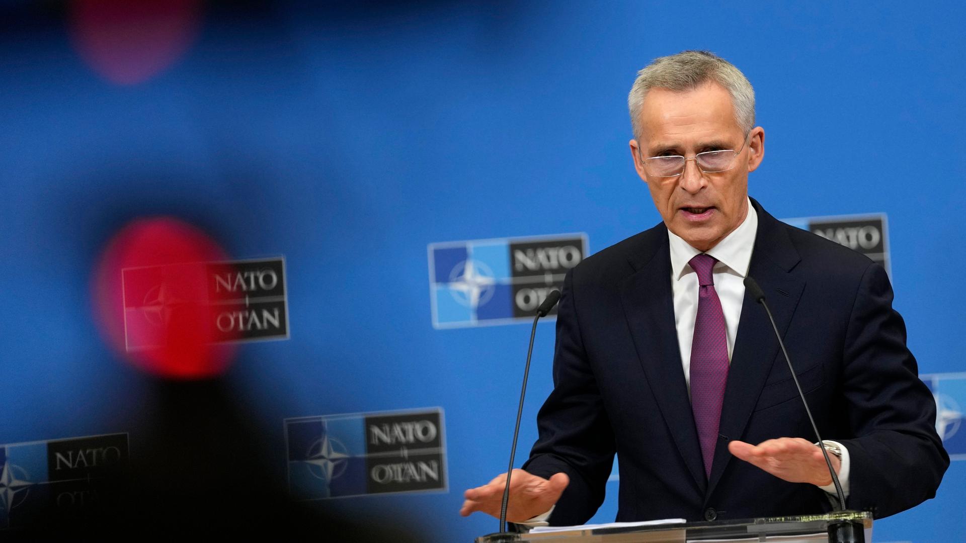 NATO-Generalsekretär Stoltenberg spricht in ein Mikrofon. Im Hintergrund ist eine blaue Wand mit Logos der NATo zu sehen