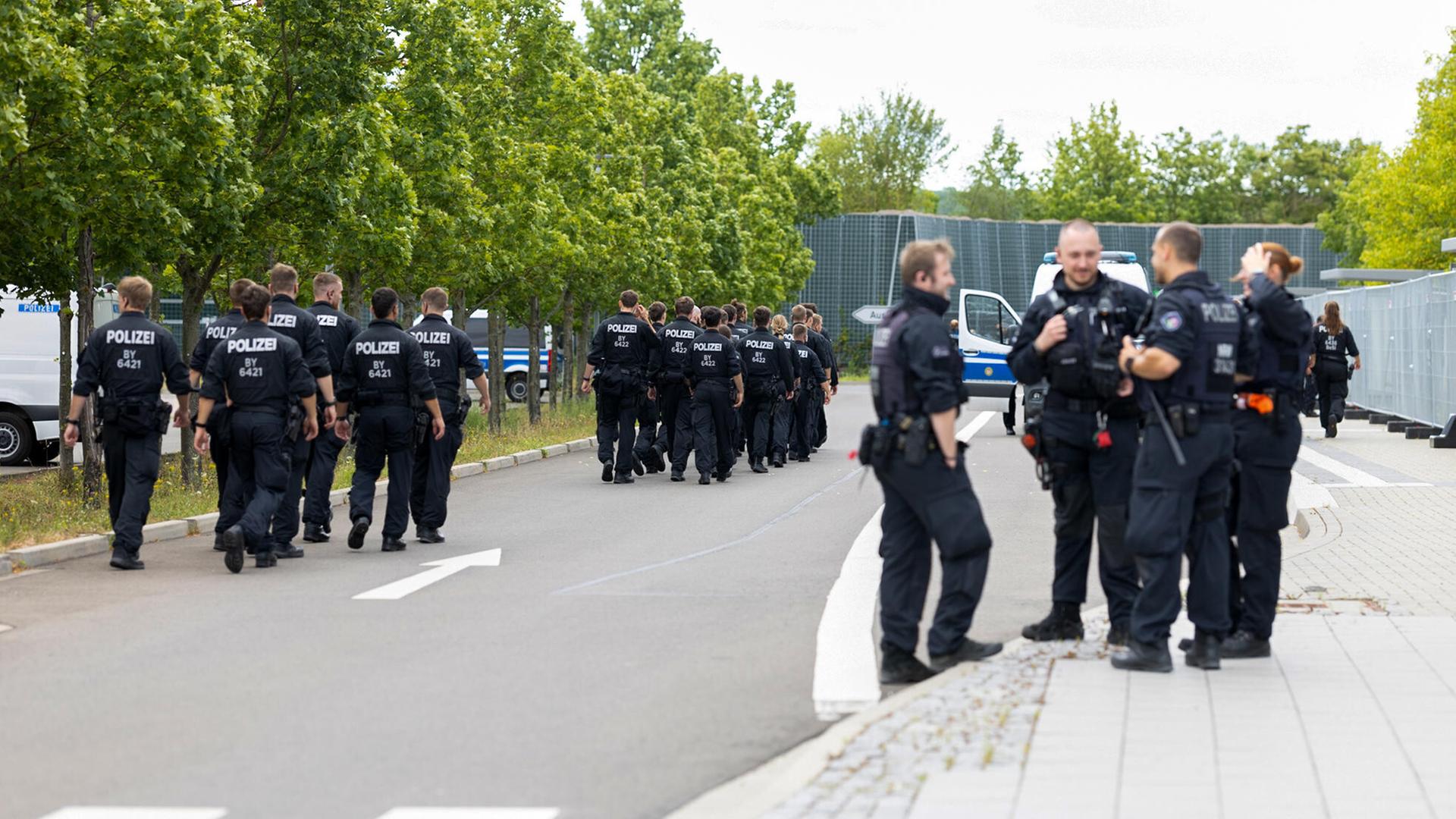 Mehrere Gruppen von Menschen in dunkler Uniform stehen laufen über einen Platz, auf ihrem Rücken steht "Polizei".