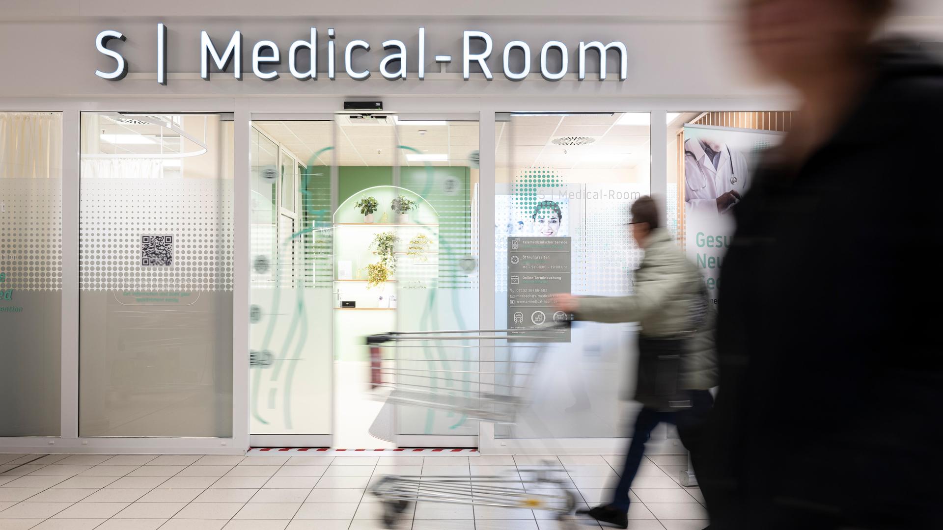 Menschen gehen in einem Kaufland-Center an einer Telemedizin-Praxis vorbei.