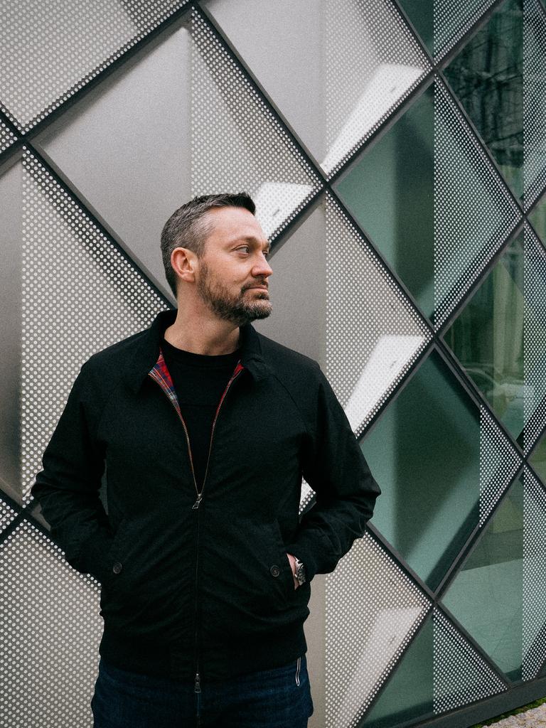 Fritz Kalkbrenner steht mit kurzem Haar und dunkler Jacke vor einer geometrisch gegliederten Wand.