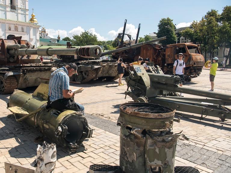 Tägliches Leben in Kiew, ein Mann liest ein Buch während er auf den Resten einer russischen Rakete sitzt, die auf dem Mykhailivska-Platz im Stadtzentrum von Kiew ausgestellt ist.