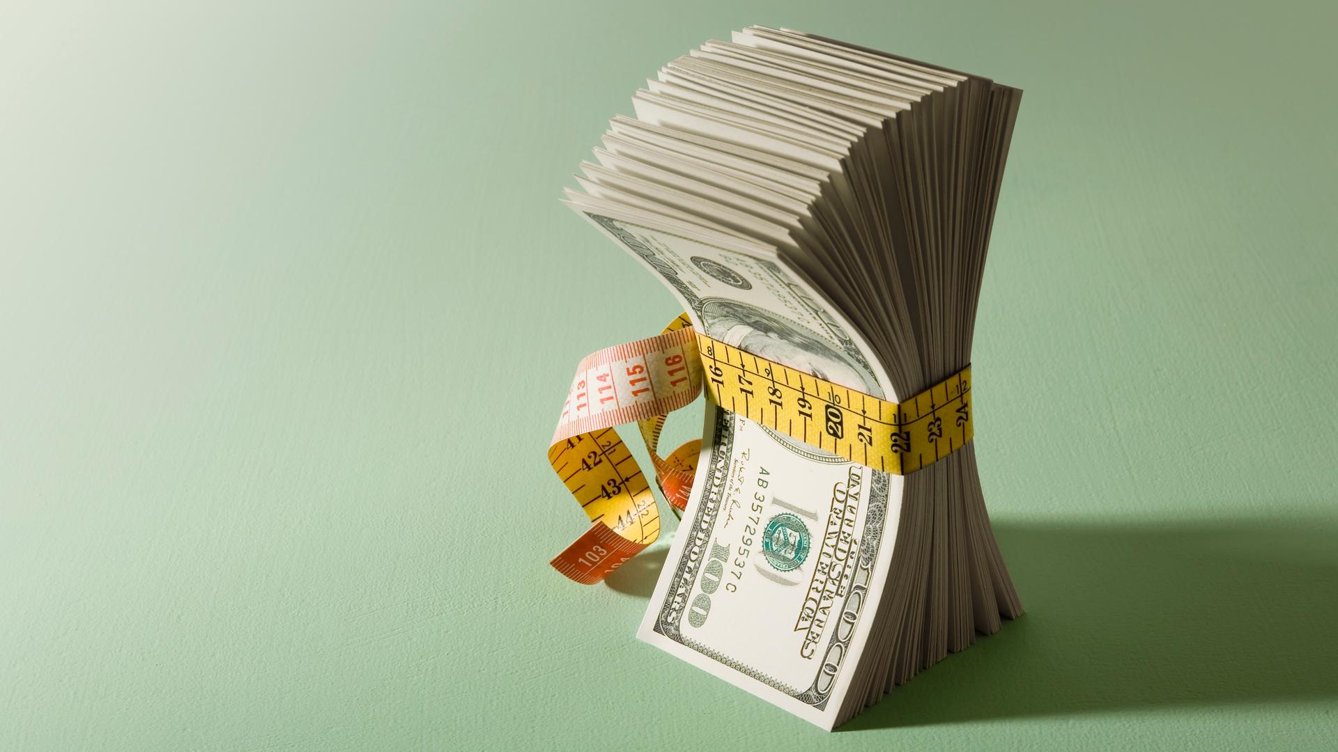 Illustration: Ein Bündel Dollarscheine, die mit einem Maßband zusammengehalten werden
