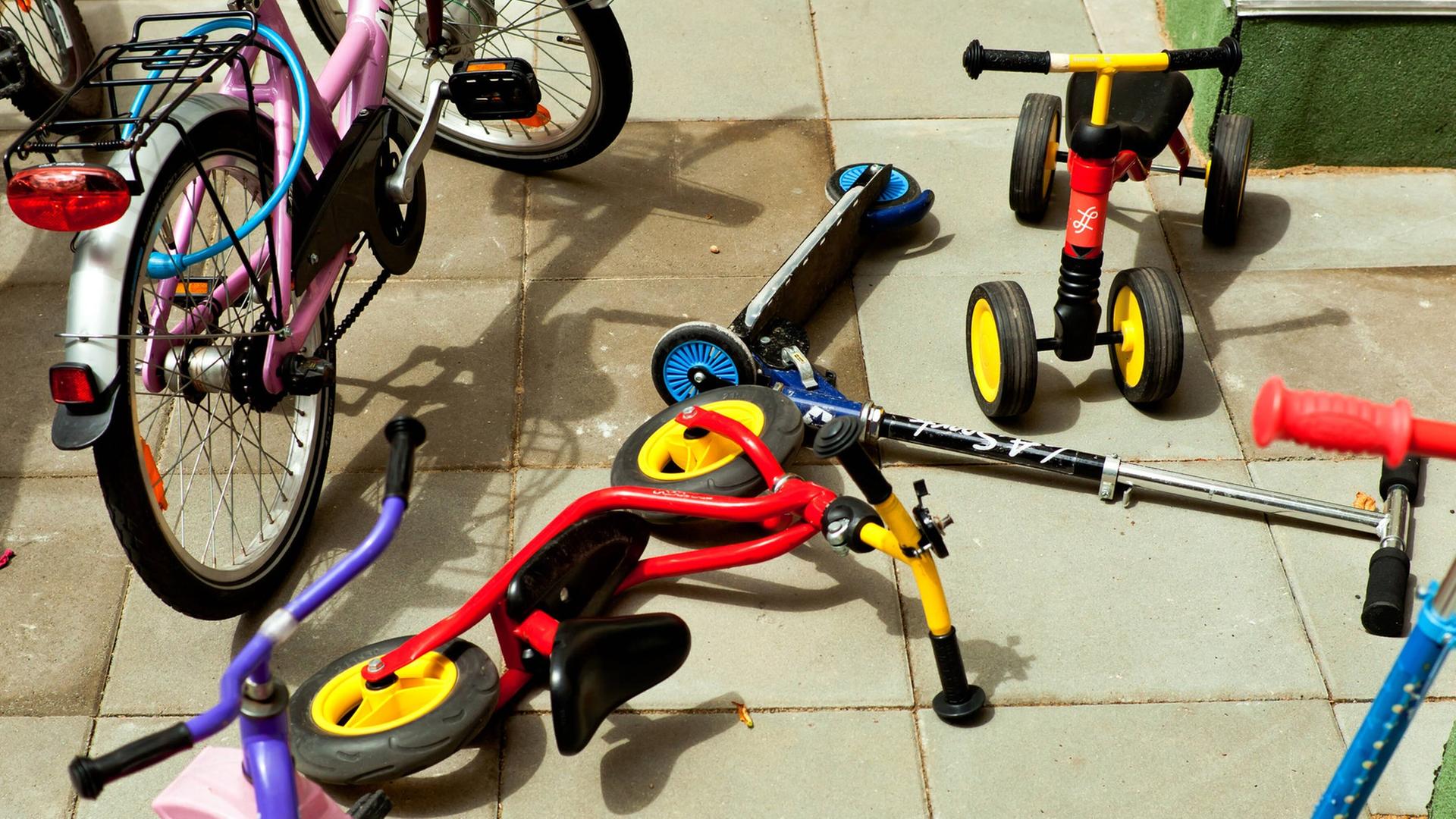 Roller, Dreiräder und kleine Fahrräder liegen durcheinander auf dem Boden einer Kita.
