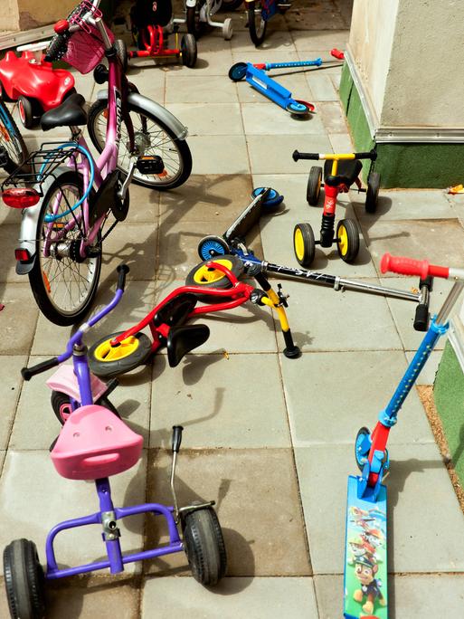 Roller, Dreiräder und kleine Fahrräder liegen durcheinander auf dem Boden einer Kita.