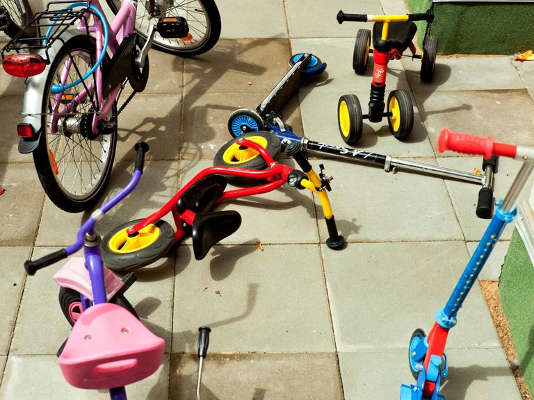 Roller, Dreiräder und kleine Fahrräder liegen durcheinander auf dem Boden einer Kita.