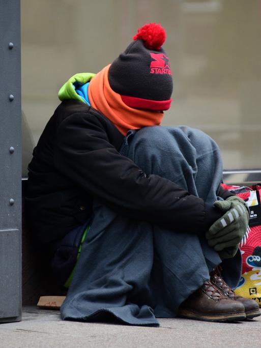 Ein warm angezogener Mann sitzt in der Innenstadt und sammelt Spenden.