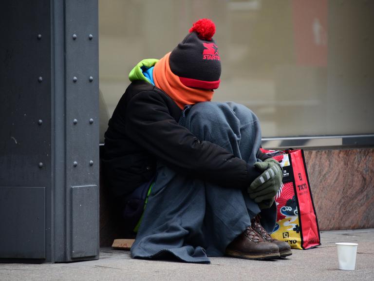 Ein warm angezogener Mann sitzt in der Innenstadt und sammelt Spenden.