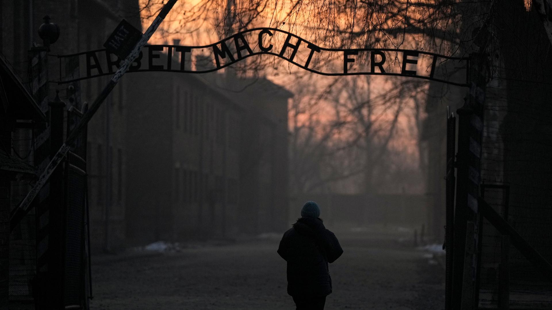 Eine Person geht zum Tor des ehemaligen deutschen Konzentrations- und Vernichtungslagers Auschwitz-Birkenau mit dem Schriftzug "Arbeit macht frei". 