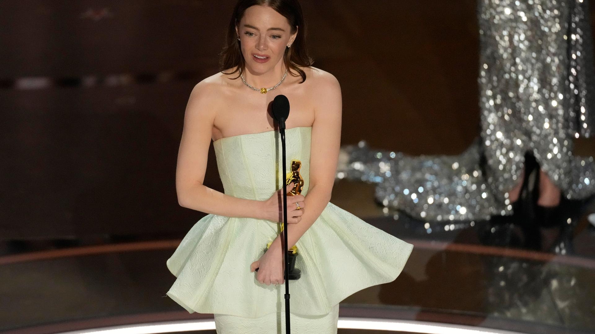 Emma Stone bei der Oscar-Verleihung im Dolby Theater in Los Angeles. Sie hält die Oscar-Statue in beiden Händen und schaut zur Seite.