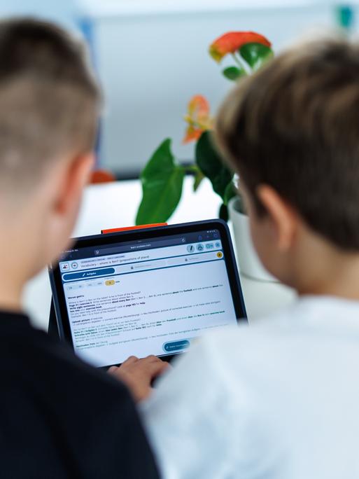 Zwei Kinder sitzen in ihrem Klassenzimmer am Tablet und schauen gemeinsam darauf. Sie sind von hinten zu sehen und damit nicht zu erkennen. Zwei Kinder sitzen in ihrem Klassenzimmer am Tablet und schauen gemeinsam darauf. Sie sind von hinten zu sehen und damit nicht zu erkennen.
