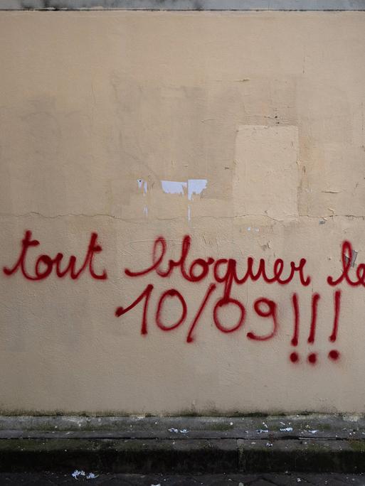 An einer Wand ist die Parole "bloquons tout" - zu deutsch "alles blockieren - mit Farbe gesprüht. 