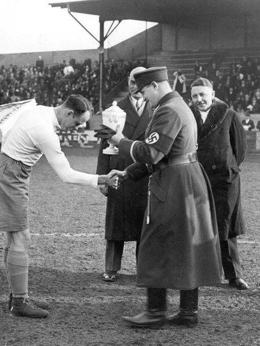 Hanne Sobek von Hertha BSC (links) erhält den Meisterschaftspokal in der Gauliga durch Gauführer Glöckler im März 1935 (vorn rechts) ca. März 1935 in Berlin. Gauliga Berlin-Brandenburg. 