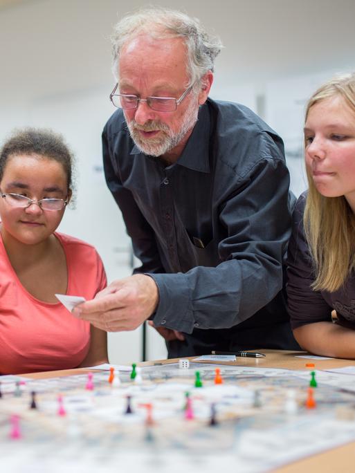 Martin Böttger (2.v.r.) erklärt Schülerinnen des Carl Bechstein Gymnasiums sein Spiel "Bürokratopoly" in Berlin, das die Realität des SED-Regimes näherbringen soll.