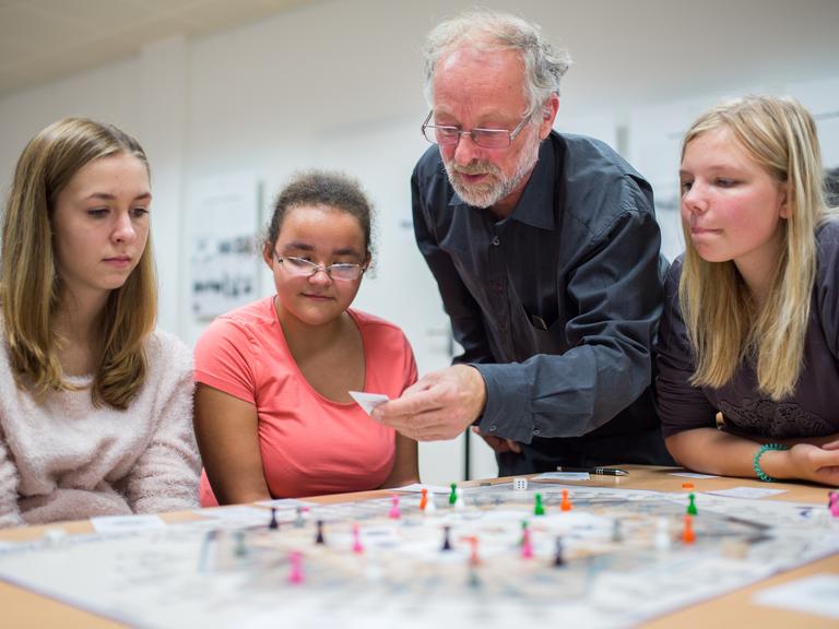Martin Böttger (2.v.r.) erklärt Schülerinnen des Carl Bechstein Gymnasiums sein Spiel "Bürokratopoly" in Berlin, das die Realität des SED-Regimes näherbringen soll.