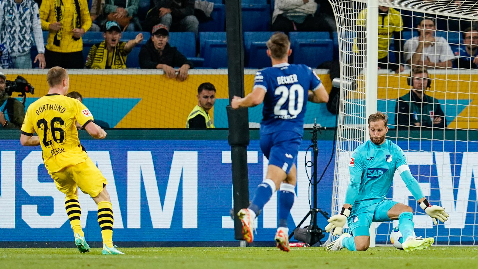 Ein Spieler in schwarz-gelbem Trikot und ein Spieler in blauem Trikot vor dem Tor. Der Torwart hat im Fallen beide Hände ausgestreckt. Ein Spieler in schwarz-gelbem Trikot und ein Spieler in blauem Trikot vor dem Tor. Der Torwart hat im Fallen beide Hände ausgestreckt.