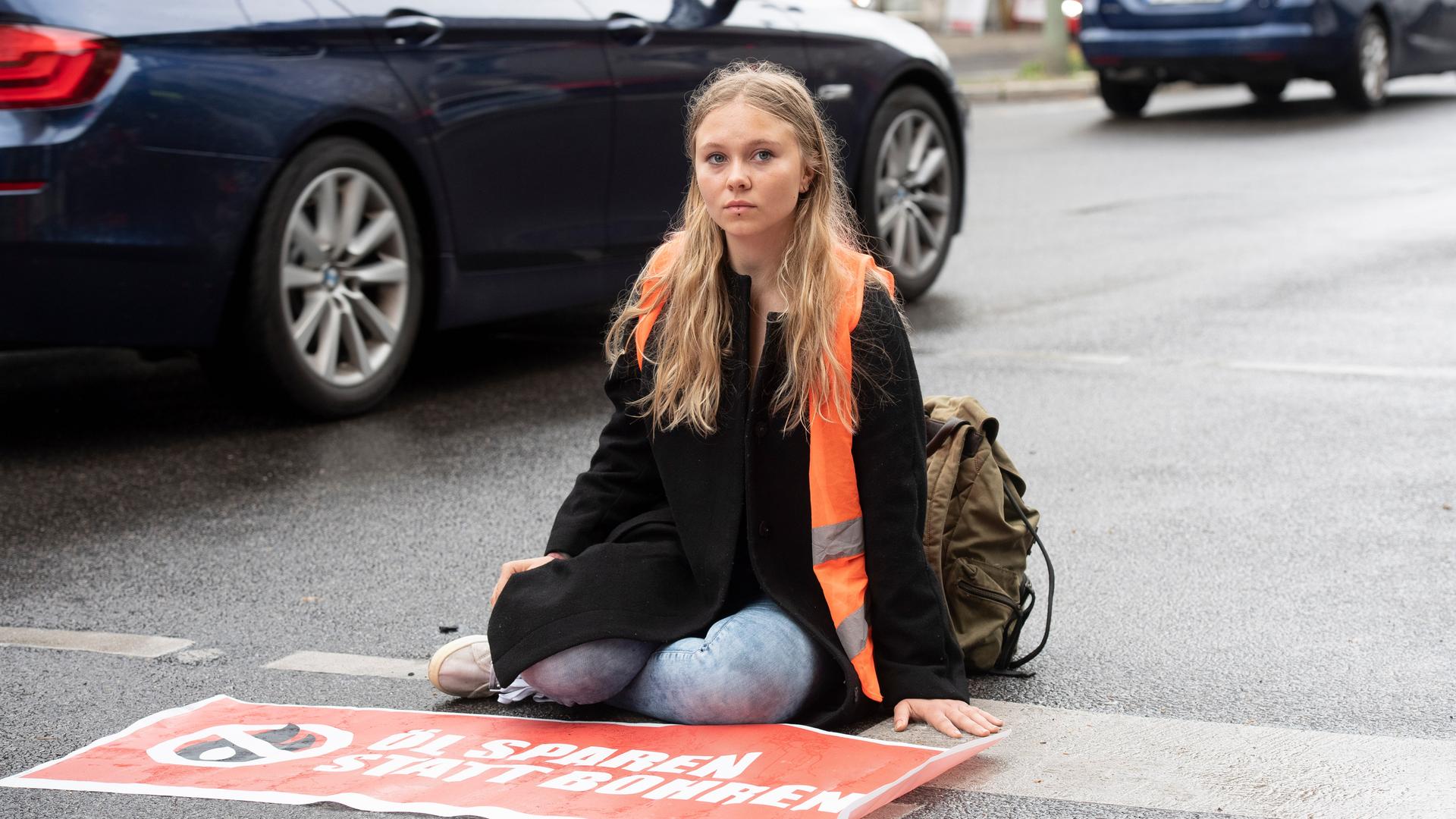 Klebeprotestlerin Aimée van Baalen sitzt festgeklebt auf einer Straße.