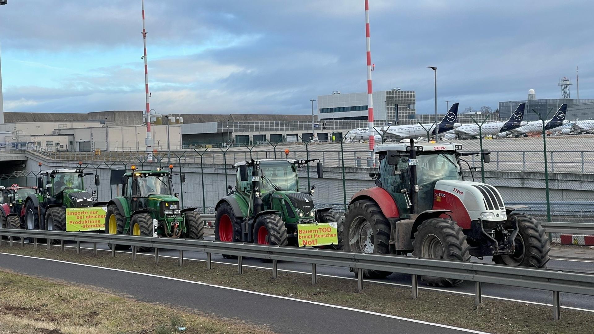 Traktoren fahren auf einer Straße am Flughafen Frankfurt vorbei. Im Hintergrund sind Flugzeuge zu sehen.