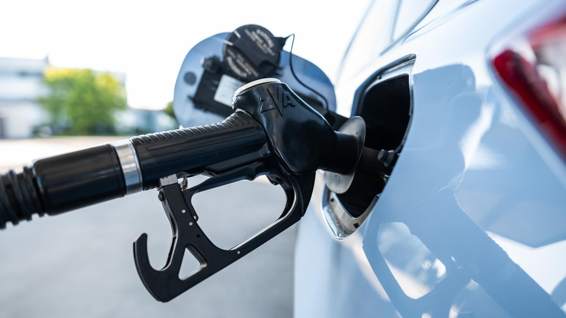 Ein Tankrüssel steckt während eines Tankvorgangs in einem Verbrenner an einer Zapfsäule einer Tankstelle.