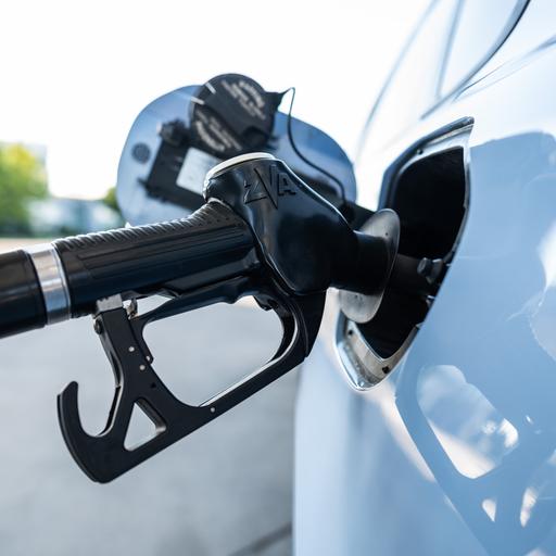 Ein Tankrüssel steckt während eines Tankvorgangs in einem Verbrenner an einer Zapfsäule einer Tankstelle.