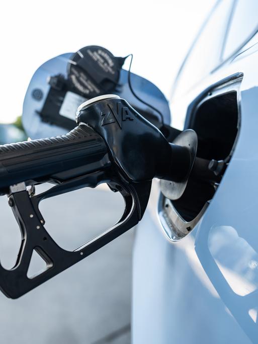 Ein Tankrüssel steckt während eines Tankvorgangs in einem Verbrenner an einer Zapfsäule einer Tankstelle.