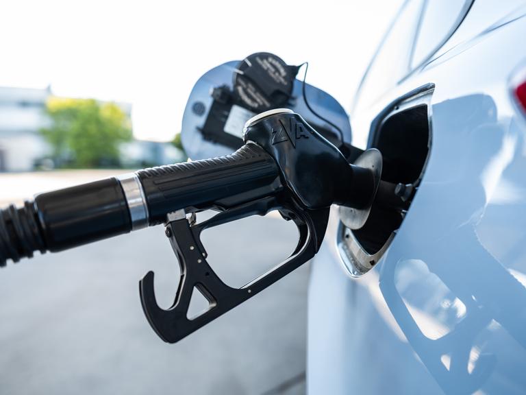 Ein Tankrüssel steckt während eines Tankvorgangs in einem Verbrenner an einer Zapfsäule einer Tankstelle.
