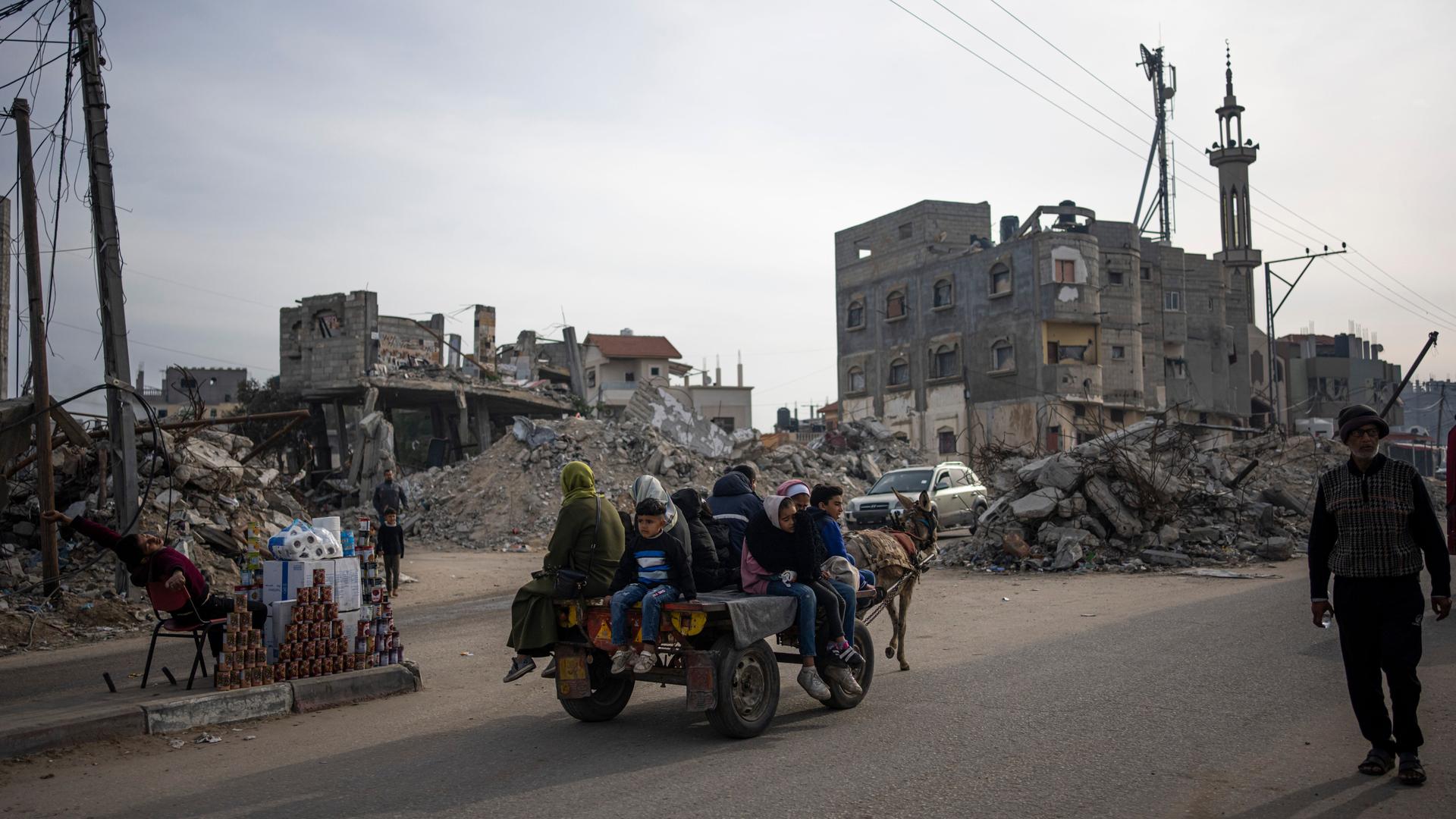 Palästinenser fahren auf einem von einem Esel gezogenen Wagen an Gebäuden vorbei, die durch einen israelischen Luftangriff zerstört wurden.