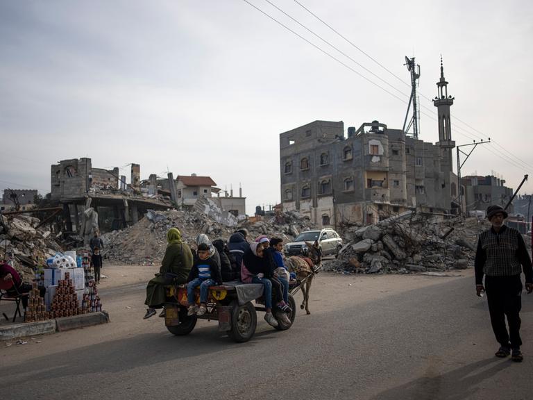 Palästinenser fahren auf einem von einem Esel gezogenen Wagen an Gebäuden vorbei, die durch einen israelischen Luftangriff zerstört wurden.