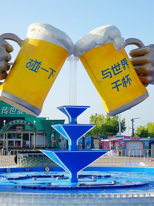 Eine große Skulptur zeigt zwei Biergläser, mit denen angestoßen wird. Das überlaufende Bier bildet in der Mitte einen Springbrunnen.