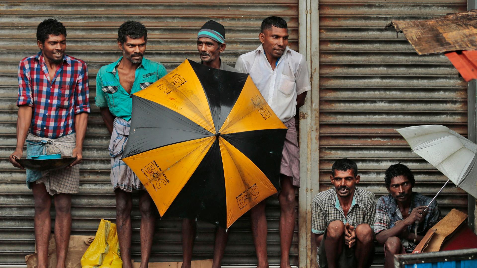 Ethnische tamilische Arbeiter aus Sri Lanka schützen sich mit Schirmen vor starkem Regen in einem Gewerbegebiet in Colombo, Sri Lanka. 