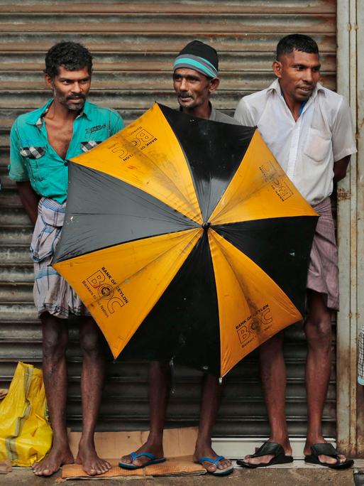 Ethnische tamilische Arbeiter aus Sri Lanka schützen sich mit Schirmen vor starkem Regen in einem Gewerbegebiet in Colombo, Sri Lanka. 