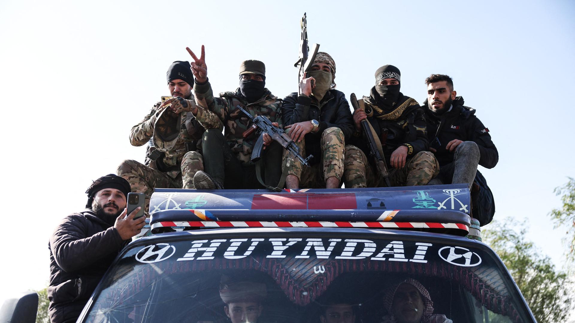 Kämpfer der syrischen Regierungstruppen sitzen auf einem Autodach. Sie sind vermummt, einer reckt ein Gewehr in die Luft. Kämpfer der syrischen Regierungstruppen sitzen auf einem Autodach. Sie sind vermummt, einer reckt ein Gewehr in die Luft.