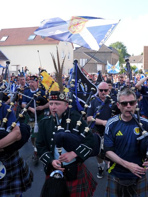 Männer in Kilts und Dudelsäcken laufen durch eine Straße. Die „Tartan Army“ nimmt vor einem Fußballspiel im Kölner Stadion an einem organisierten Marsch zum Stadion teil. 
