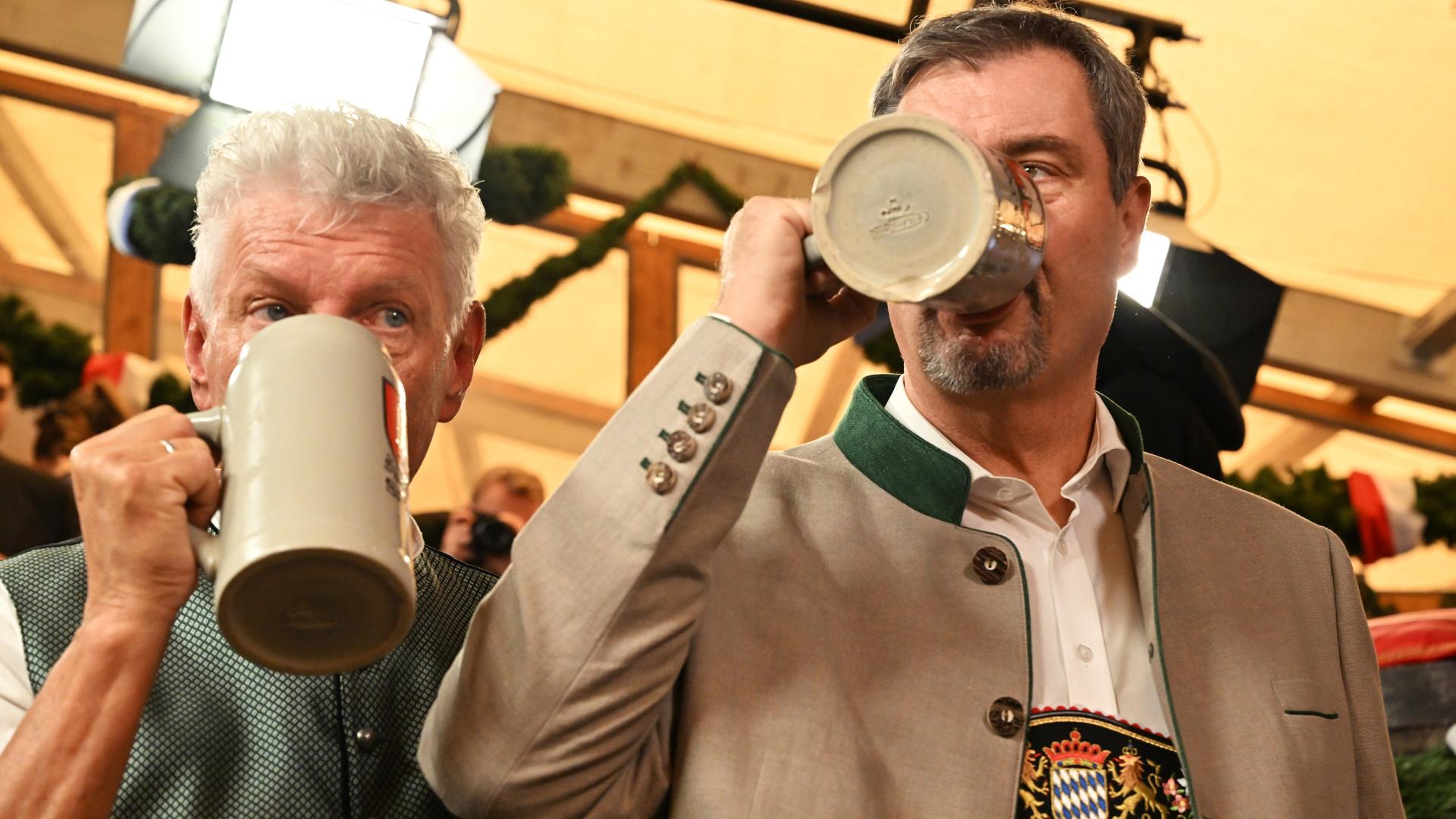 Oberbürgermeister Dieter Reiter und Bayerns Ministerpräsident Markus Söder stehen nebeneinander. Ihre Gesichter sind von großen Bierkrügen verdeckt, aus denen sie trinken. Oberbürgermeister Dieter Reiter und Bayerns Ministerpräsident Markus Söder stehen nebeneinander. Ihre Gesichter sind von großen Bierkrügen verdeckt, aus denen sie trinken.