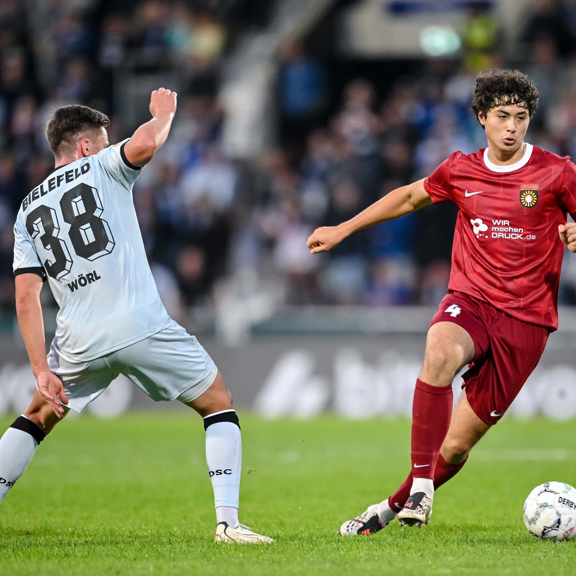 Marius Woerl im weißen Trikot von Arminia Bielefeld und Franz Bleicher im roten Trikot von Sonnenhof Großaspach kämpfen um den Ball.